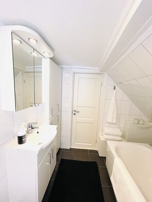 Un baño con lavamanos, espejo, tocador, una puerta y una bañera.