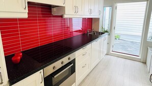 A modern kitchen with white cabinets, a black countertop, and red backsplash tiles. - Central Economic Stavanger (Stavanger)