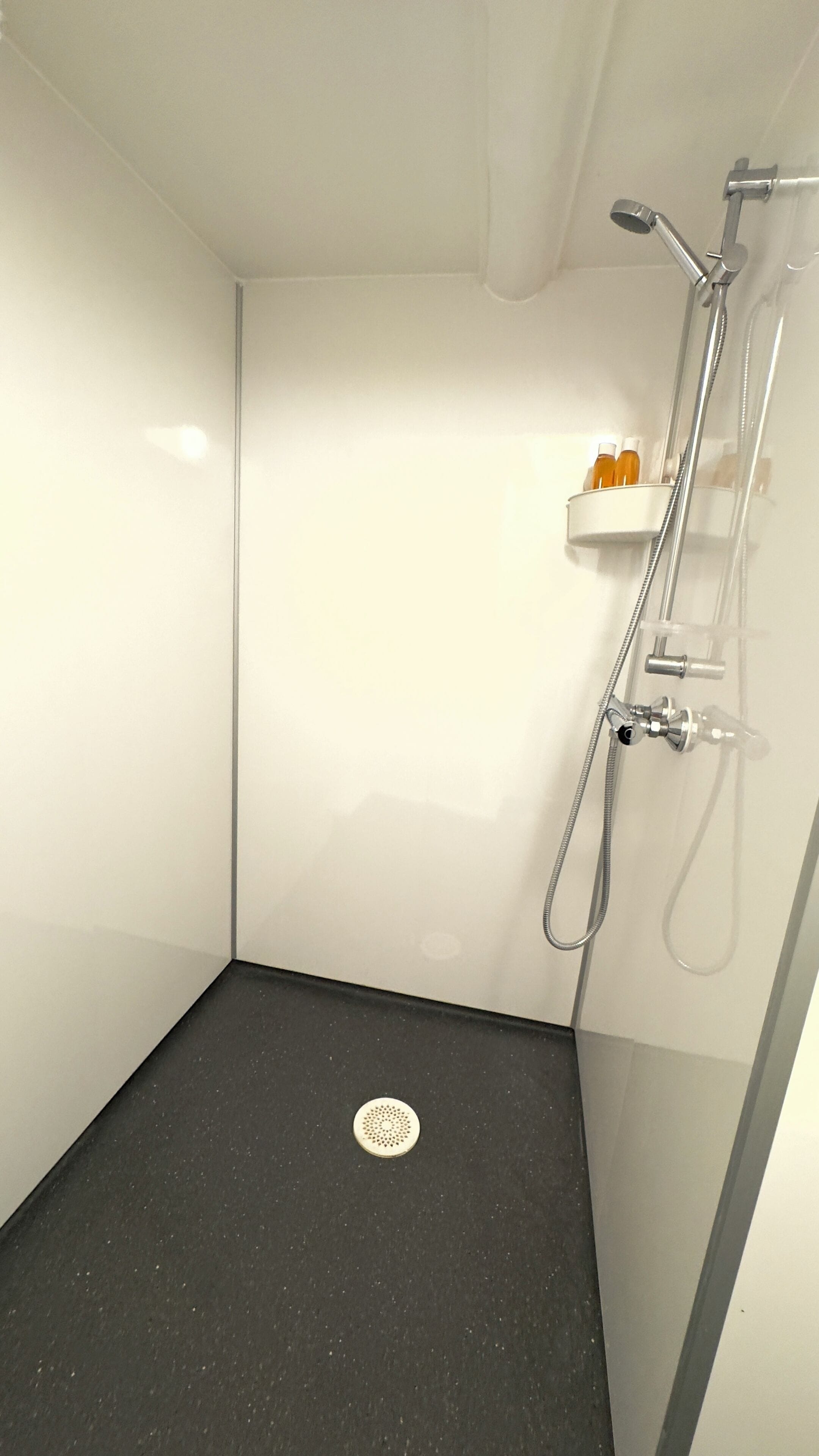 A small, modern shower room with a black floor, white walls, and a chrome shower head.
