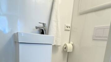 A modern bathroom with a white sink, mirror, toilet, and a small trash bin.