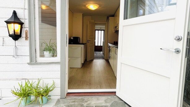 A house entrance with a stone-paved porch, a white door, and a kitchen visible through an open door. - Central Economic Stavanger (Stavanger)