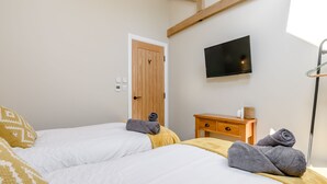 Un dormitorio con dos camas, un aparador de madera, un televisor en la pared y una puerta.