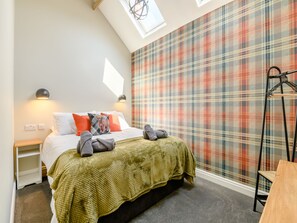 A bedroom with a bed, a window, a wall with a plaid pattern, a bedside table, and a hanging rack.