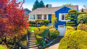 A blue house with a well-maintained garden, a visible mailbox, and a clear sky. - Magnolia on the Hill (Seattle)