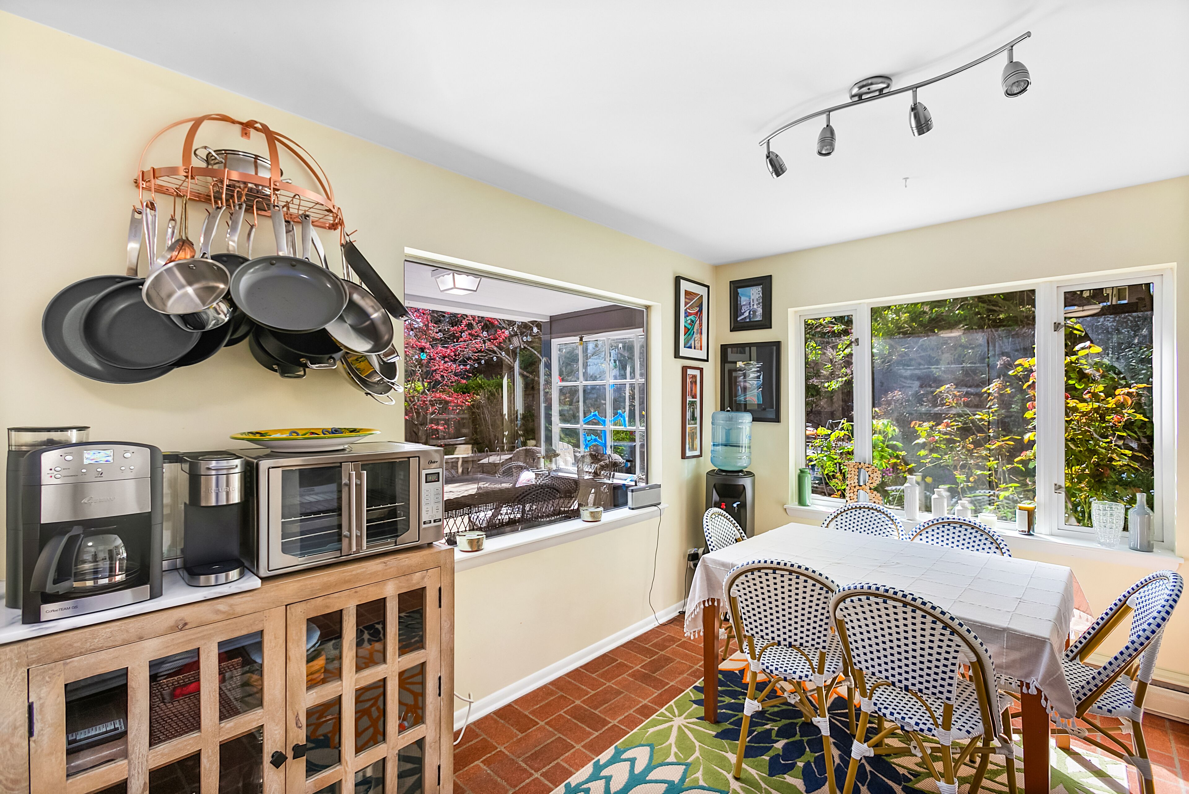 Una cocina con zona de comedor, que incluye cafetera, tostadora, microondas y utensilios colgantes.