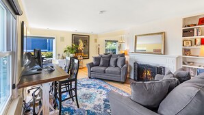 A modern living room with a fireplace, a grey sofa, a dining area with a wooden table, and a bookshelf. - Magnolia on the Hill (Seattle)