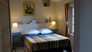 Quarto bem arrumado com cama, duas mesas de cabeceira, abajur, quadro e janela com cortinas.