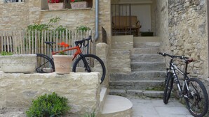 Uma escadaria de pedra leva a uma porta de madeira, com uma bicicleta estacionada nos degraus e um vaso de planta no patamar.