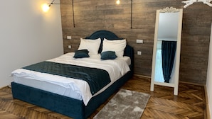 A modern bedroom with a wooden wall, a bed with dark blue bedding, two wall-mounted lights, and a mirror with a hanging light fixture. - 1793 Margarethengasse Guesthouse (Sibiu)