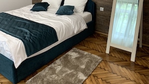 A modern bedroom with a wooden wall, a bed with white and dark blue bedding, a mirror, and a herringbone-patterned floor. - 1793 Margarethengasse Guesthouse (Sibiu)