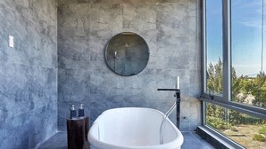 A modern bathroom with a freestanding bathtub, a round mirror, and a window offering a view of greenery. - Spacious 1bdr Perfect For Romantic Weekend Seaview (Da Nang)