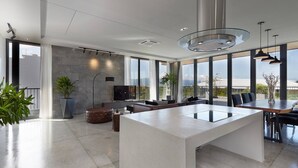 A spacious living area with a large island table, comfortable seating, a flat-screen TV, and large windows offering a city view. - Spacious 1bdr Perfect For Romantic Weekend Seaview (Da Nang)