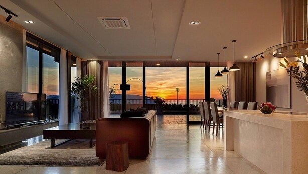 A spacious living area with a large window offering a sunset view, a modern kitchen with a bar, and a seating area with a sofa and chairs. - Spacious 1bdr Perfect For Romantic Weekend Seaview (Da Nang)