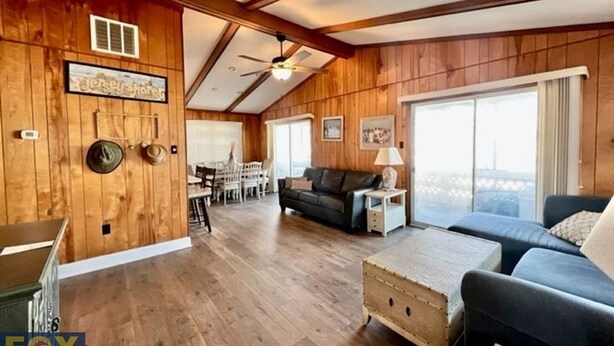 Un vaste salon aux murs en bois et doté d’un ventilateur de plafond, un coin repas avec une table et des chaises, et une grande fenêtre offrant une vue dégagée.