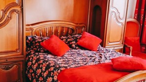 A bed with a floral bedspread and red pillows, a wooden headboard, and a red rug. - Grande Maison Familiale Proche Paris /roissy/le Bourget (Le Blanc-Mesnil)