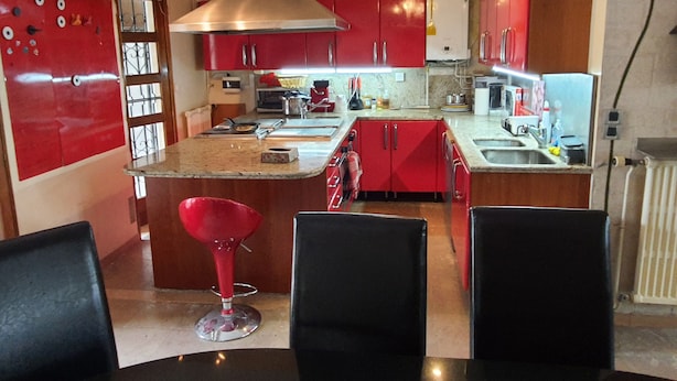 A compact kitchen with red cabinets, a central island, and a red bar stool. - Grande Maison Familiale Proche Paris /roissy/le Bourget (Le Blanc-Mesnil)