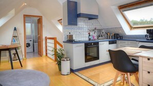 A modern kitchen with a built-in oven, a dining area with a table and chairs, and a view through a skylight. - Les Palmiers D'armor (Penvénan)