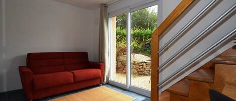 Una habitación con sofá rojo, escalera de madera y vista a un jardín a través de un ventanal.