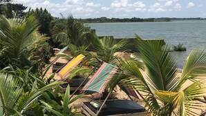 Vista de la playa con hamacas y palmeras, con vista a una masa de agua tranquila.