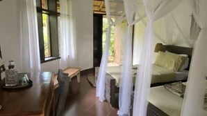 Una habitación con una cama bajo un dosel, un escritorio de madera con una silla y una ventana con cortinas.
