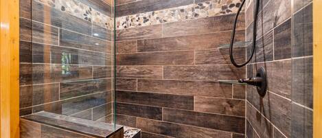 Ducha con azulejos oscuros y puerta de vidrio, cabezal de ducha visible y un estante pequeño.