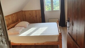 Un dormitorio con cama de madera, ventana con cortinas y vista a zonas verdes.