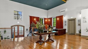 A spacious room with a wooden floor, a dining table with chairs, red curtains, and a staircase with a railing. - Sherlock @The Vestry on Read (Columbia)