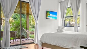 Ein Schlafzimmer mit Bett, Blick auf einen tropischen Strand und einer Hängematte davor.