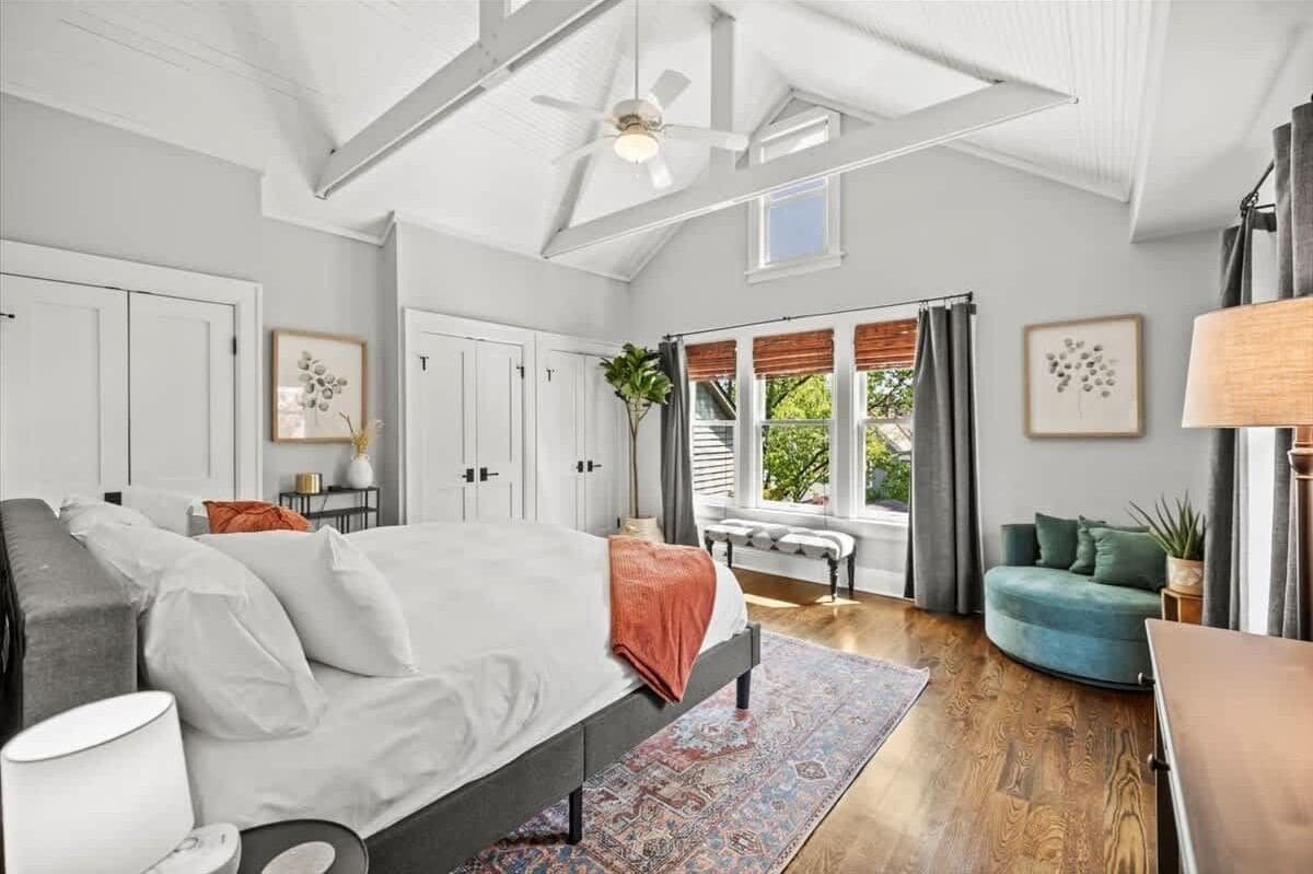 Une chambre spacieuse avec un grand lit, un ventilateur de plafond et une vue sur l’extérieur par une fenêtre.