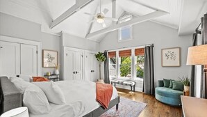 A spacious bedroom with a large bed, a ceiling fan, and a view of the outdoors through a window.
