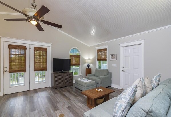 A living room with a ceiling fan, a television, a sofa, a coffee table, and a lamp.