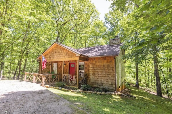 Cozy cabin surrounded by lush greenery, featuring a charming porch and a prominent red door.