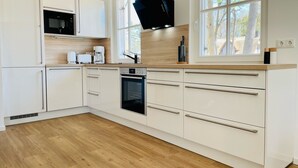 A modern kitchen with white cabinetry, a built-in oven, a microwave, and a black range hood.