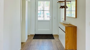 A hallway with a wooden floor, a white door, a black doormat, and a wooden vanity with a mirror.