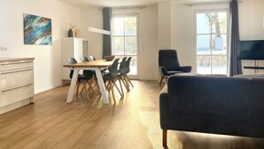 A modern living room with a dining area, wooden flooring, and large windows.