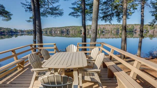 Eine Holzterrasse mit Tisch und Stühlen mit Blick auf einen ruhigen See, umgeben von Bäumen.