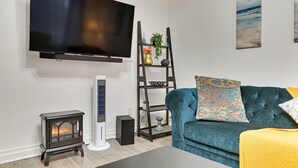 A modern living room with a flat-screen TV, a wood-burning stove, a blue sofa, and a decorative shelf. - Walk to Downtown Albany: Ten Broeck Triangle Apt! (Albany)