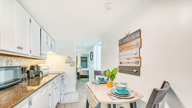 A modern kitchen with white cabinets, a granite countertop, and a dining area with a table set for two. - Walk to Downtown Albany: Ten Broeck Triangle Apt! (Albany)