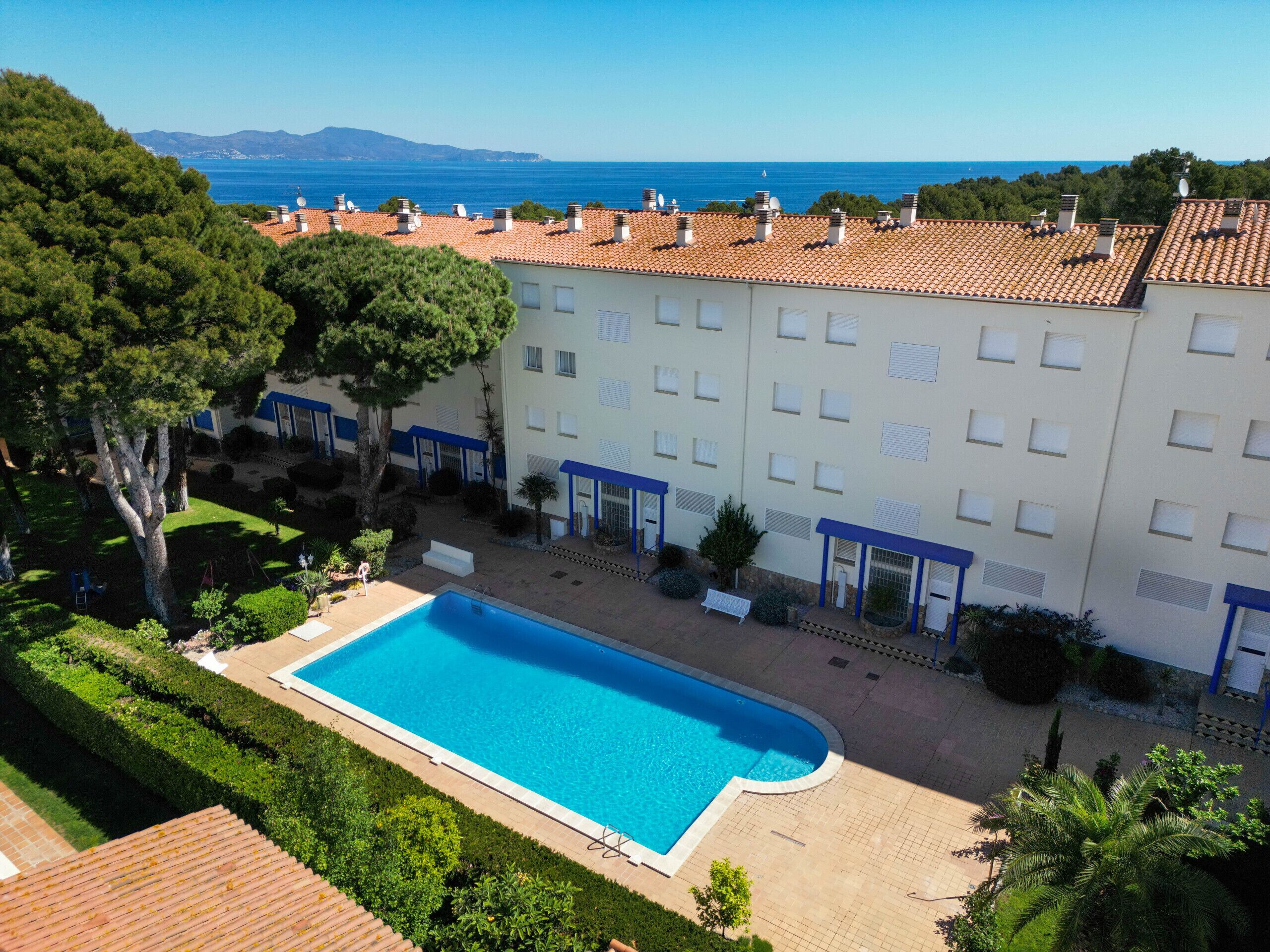 A hotel with a swimming pool, terracotta roofed buildings, and a view of the sea.