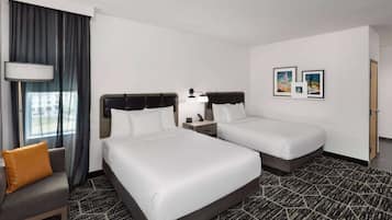 Una habitación de hotel con dos camas, un sofá, una lámpara y cuadros enmarcados en la pared.