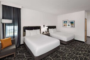 A hotel room with two beds, a sofa, a lamp, and framed pictures on the wall.
