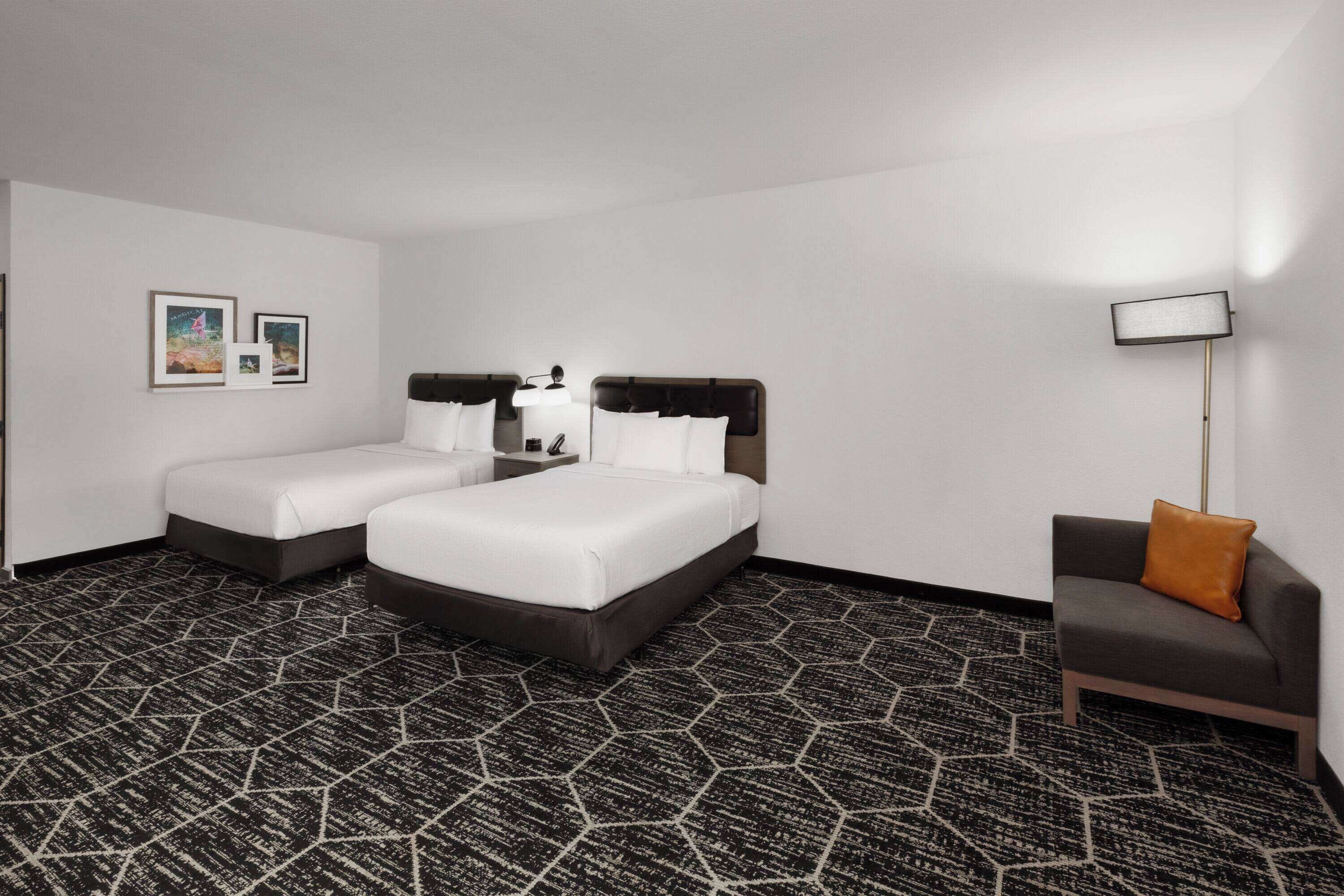 A hotel room with two beds, a sofa, a lamp, and a patterned carpet.
