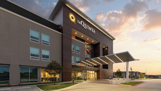 A modern hotel with a prominent 'LaQuinta' sign, large windows, and a covered entrance area. - La Quinta Inn & Suites by Wyndham Austin Parmer/Tech Ridge (Austin)