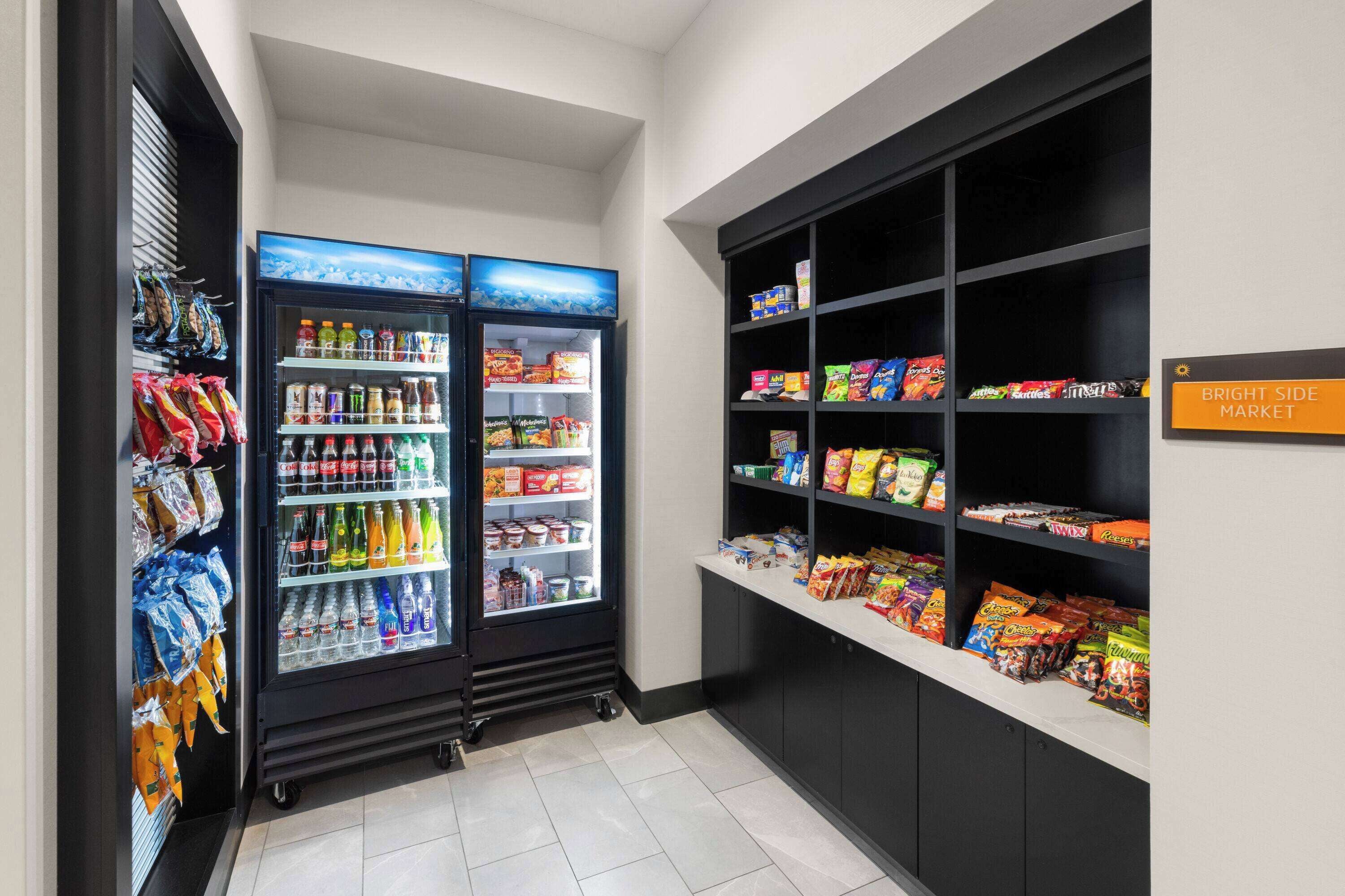 Uma área de venda automática com lanches e bebidas, com dois refrigeradores cheios de bebidas e petiscos, e prateleiras com snacks embalados.