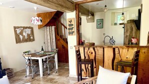 A rustic dining area with a wooden table and chairs, a staircase, and a kitchen area with wooden accents. - Former presbytery just renovated, 3 stars (Bénarville)