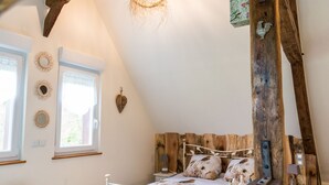 A cozy bedroom with a sloped ceiling, a bed with floral bedding, wooden headboard, and a rustic wooden beam. - Former presbytery just renovated, 3 stars (Bénarville)