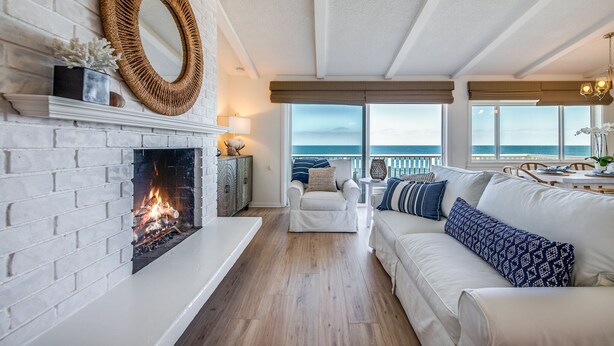 Ein Wohnzimmer mit Kamin, weißen Ziegelwänden, einem weißen Sofa und Meerblick.
