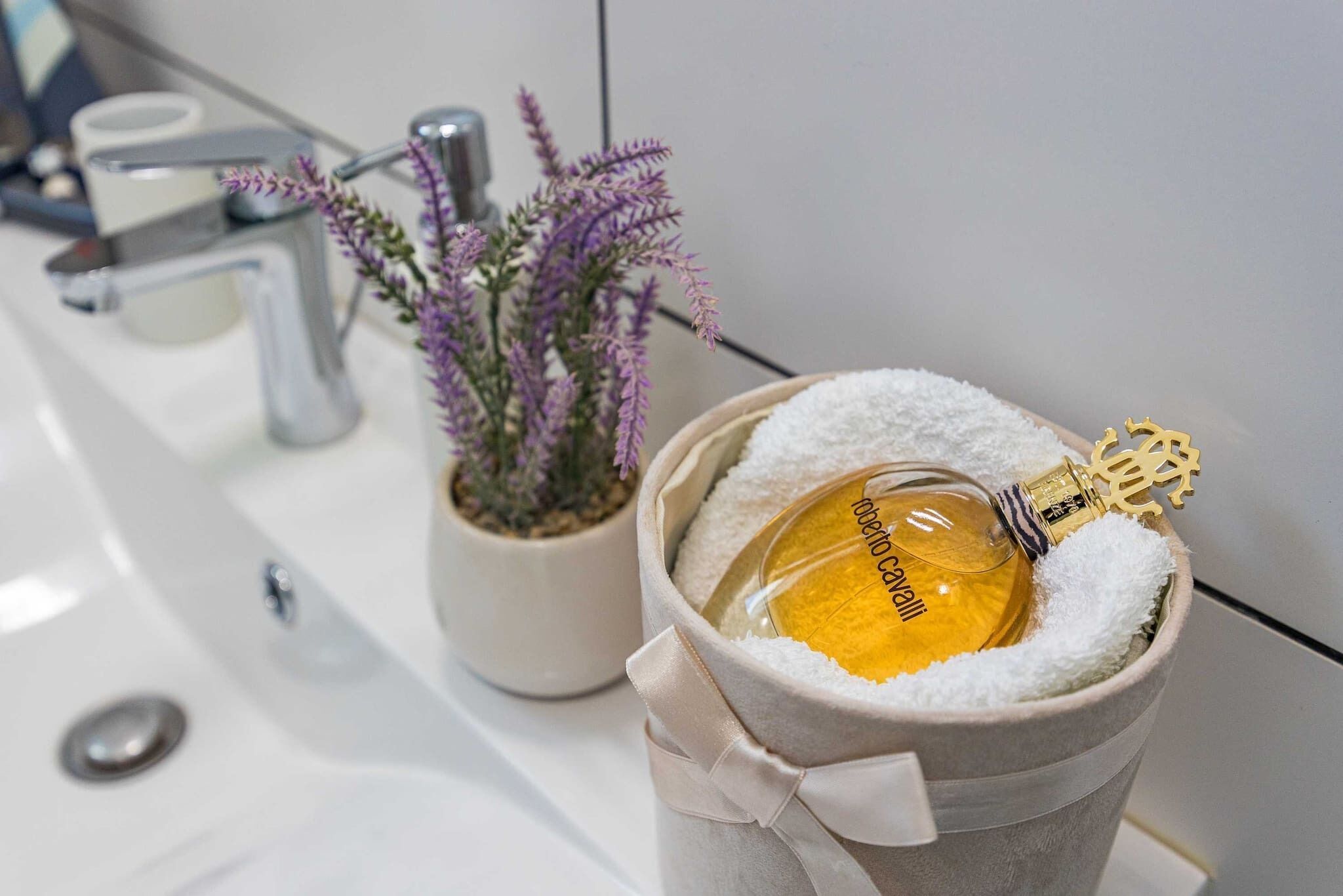 Een badkamermeubel met een wastafel, een pot lavendel en een parfumfles in een beklede houder.