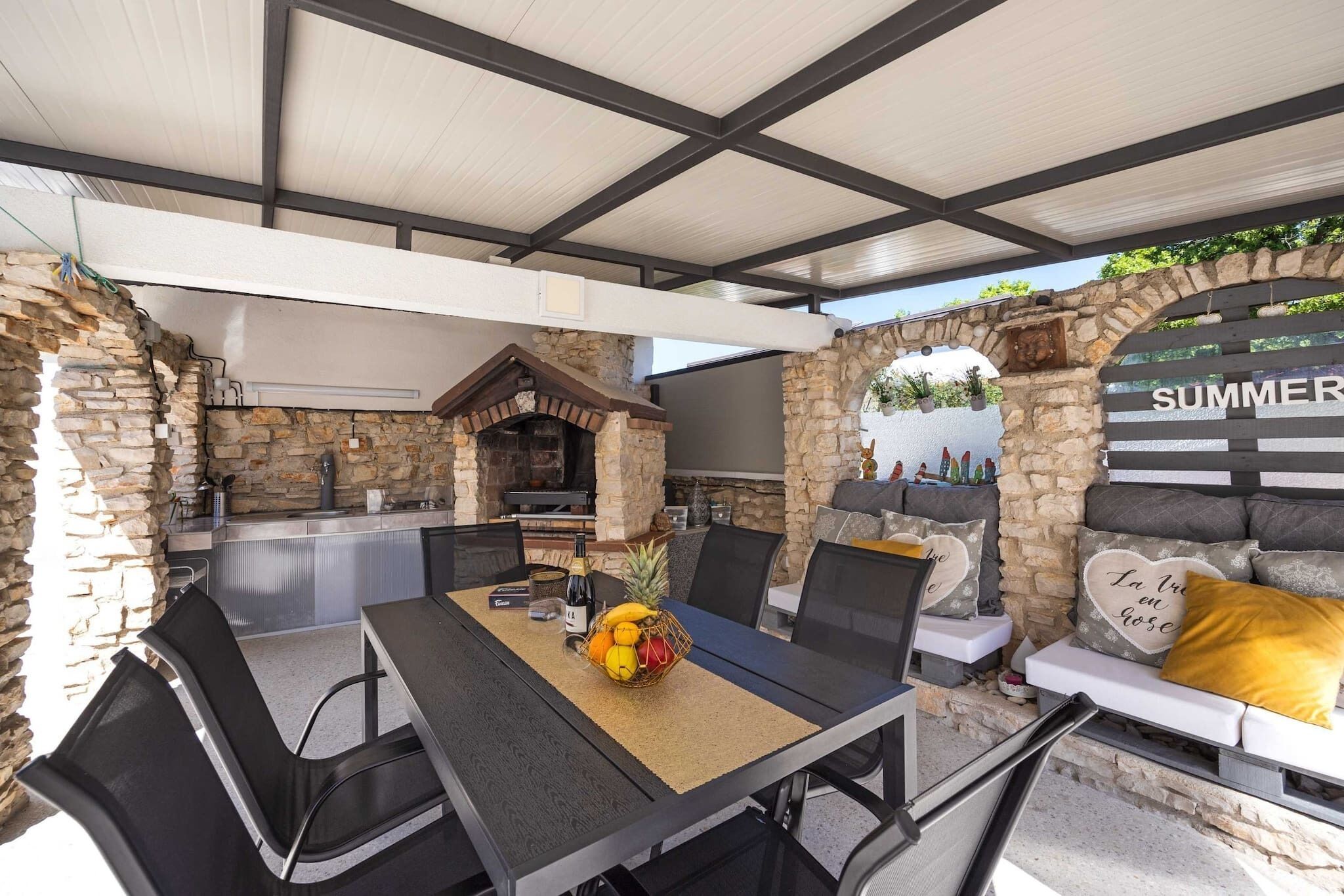 An outdoor patio with stone walls, a grill, and a seating area with cushions.