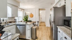 Una cocina moderna con armarios blancos, un refrigerador de acero inoxidable, un microondas y una encimera de granito.